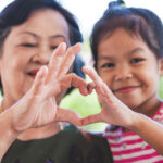 Asian grandmother and little child girl making heart shape with hands together with love